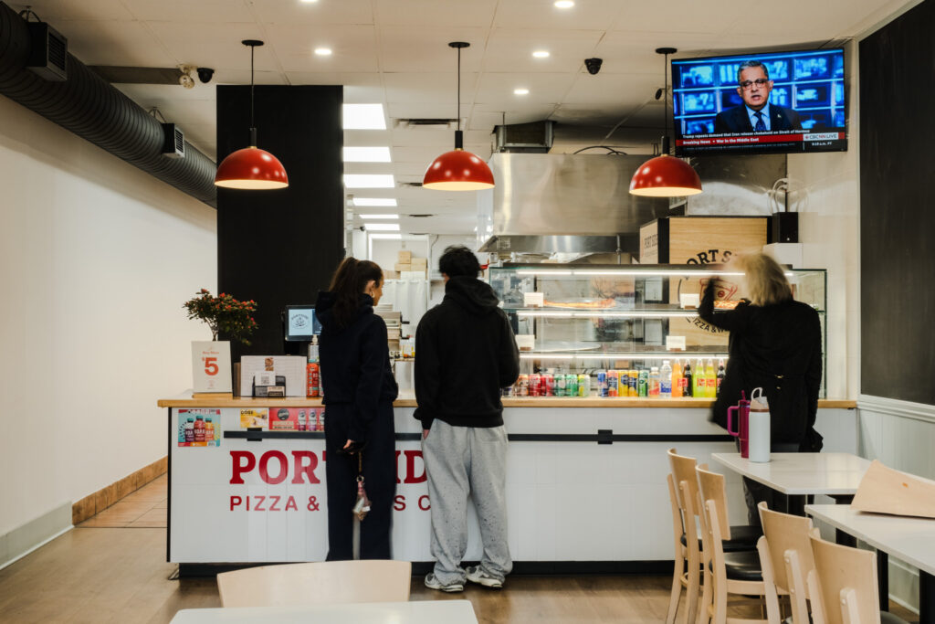 Customers ordering at the white-tiled service counter under red dome pendants — Portside Pizza & Wings, Port Credit — Studio Kimi Interior