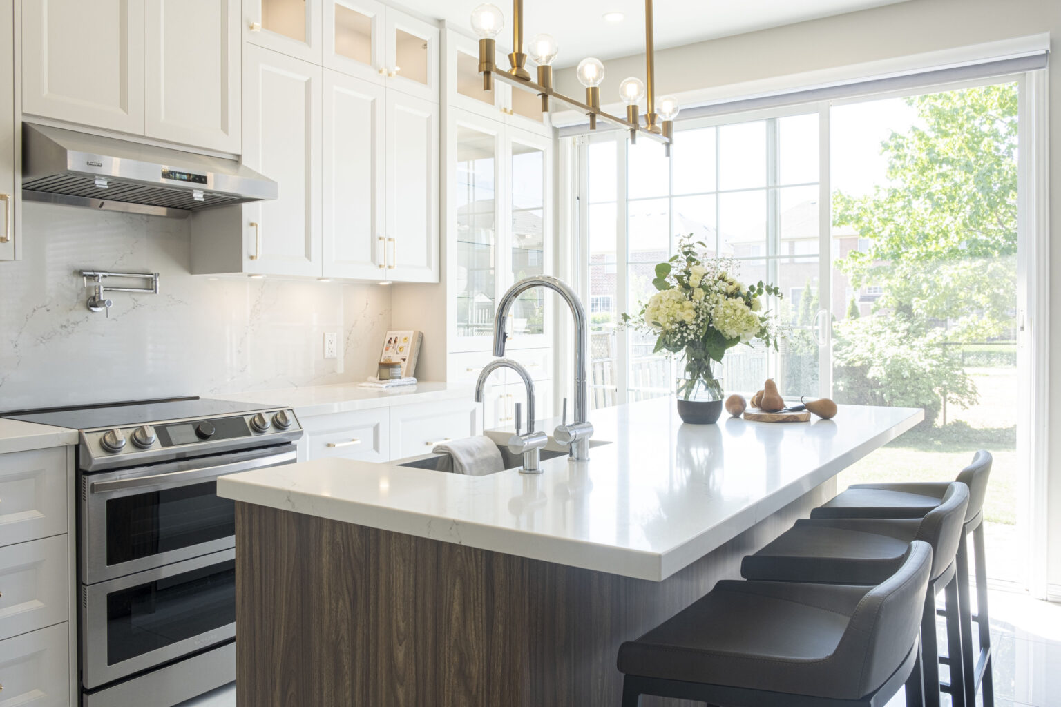 Walnut kitchen island and range under a linear chandelier