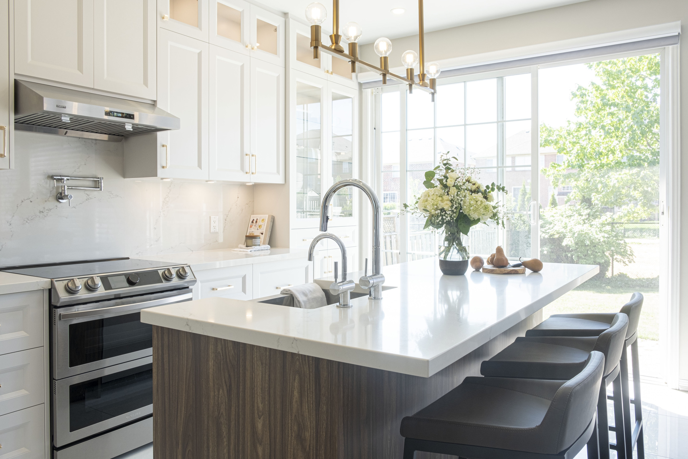 Walnut kitchen island and range under a linear chandelier